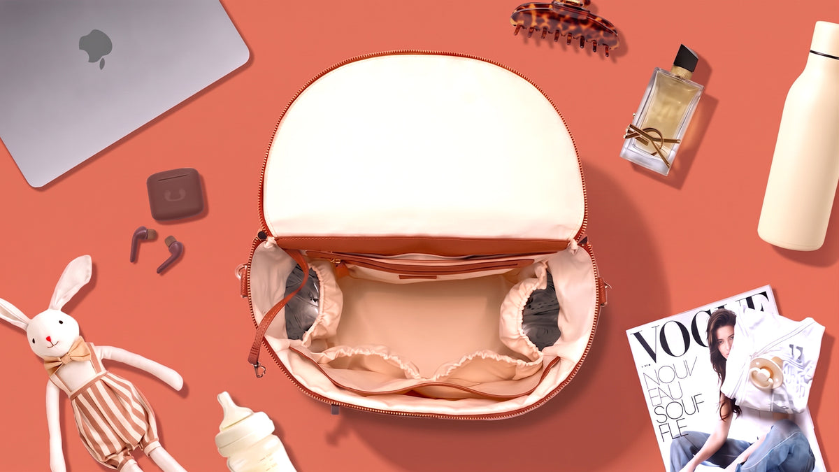 Le sac L'Iconique ouvert et vide, entouré d'un ordinateur, d'un biberon, d'un doudou, d'un parfum et d'une gourde