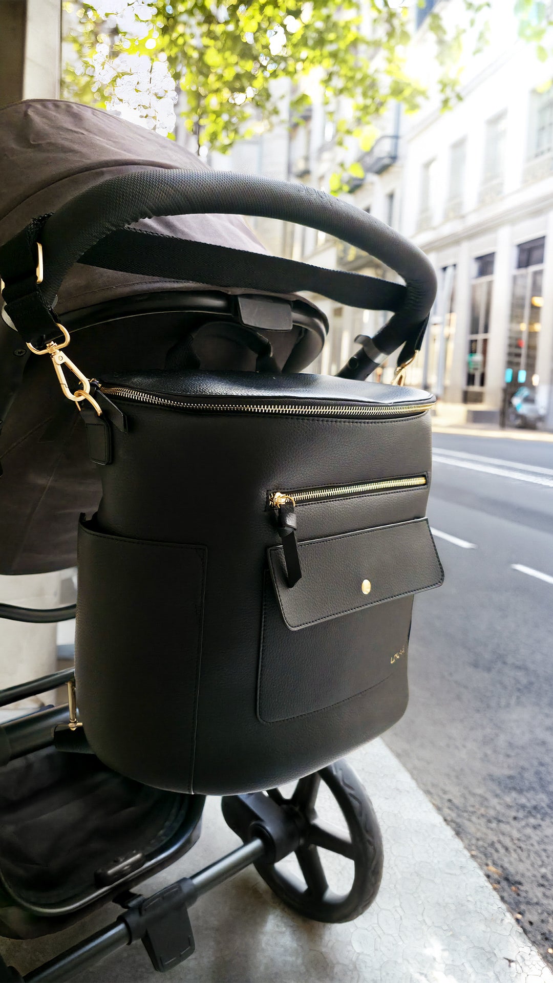 Sac à langer luxe noir LOU·VE en cuir vegan, accroché à une poussette, élégant et pratique pour les sorties avec bébé